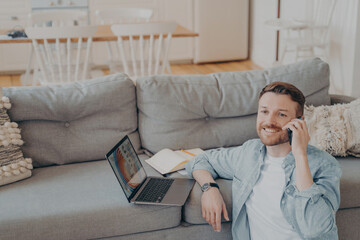 Young male office worker working from home talking on phone with his co-worker