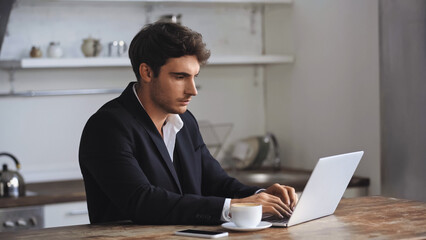 freelancer using laptop near smartphone and cup of coffee on desk.