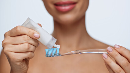 cropped view of cheerful young woman squeezing toothpaste on toothbrush isolated on white.
