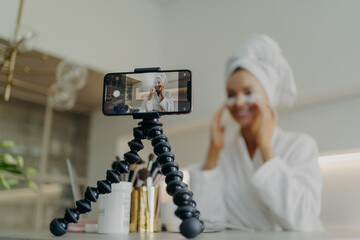 Smartphone screen with female beauty blogger in bathrobe recording video about skin care for her...