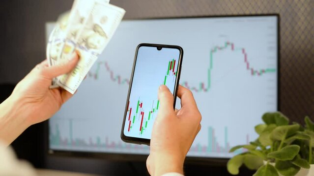 Business, finance, trading, investment and technology. Close-up of trader investor analyzing stock exchange chart on mobile phone and throwing money while sitting at his workplace.
