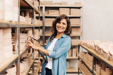 Fototapeta na wymiar Cheerful ceramist smiling at the camera in her shop