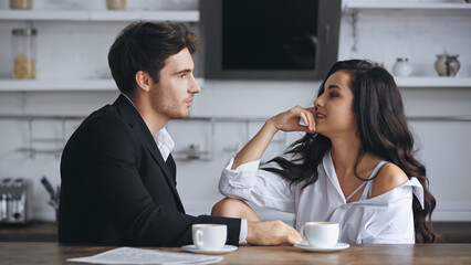 businessman talking with sensual girlfriend in white shirt near cups of coffee.
