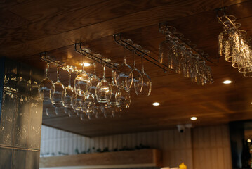 Stylish glasses for various alcoholic beverages hang over the bar in a modern restaurant. Glasses...