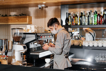 A masked barista prepares an exquisite delicious coffee at the bar in a coffee shop. The work of restaurants and cafes during the pandemic.