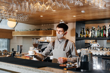 A masked barista exquisitely serves ready-made coffee in a modern cafe during a pandemic. Serving ready-made coffee to a client in a cafe.