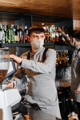 A masked barista prepares an exquisite delicious coffee at the bar in a coffee shop. The work of restaurants and cafes during the pandemic.