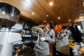 Two masked baristas prepare exquisite delicious coffee at the bar in the coffee shop. The work of restaurants and cafes during the pandemic.