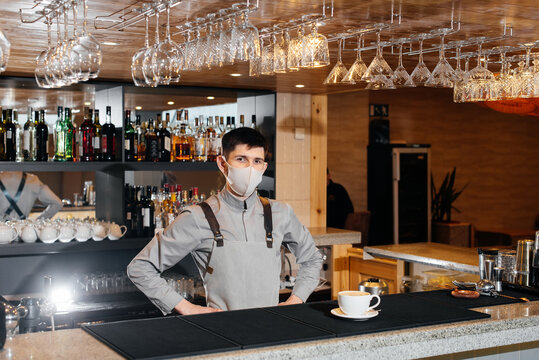 A masked barista exquisitely serves ready-made coffee in a modern cafe during a pandemic. Serving ready-made coffee to a client in a cafe.