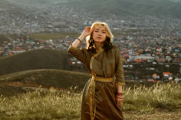 Fotobehang Young Mongolian woman wears traditional golden deel dress. Ulaanbaatar in background at sunset. © Jan