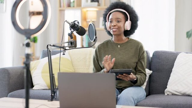 Cool afro influencer, journalist or podcast host using a digital tablet, talking into microphone, broadcasting news and wearing headphones. Excited woman using technology to promote on air from home