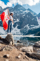 A woman with Poland flag is standing on the shore of a lake. Morskie Oko