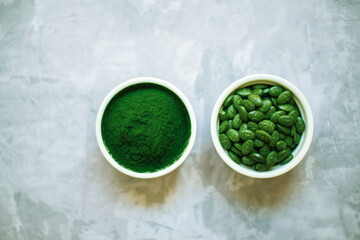 spirulina powder and tablets in white plates on concrete background