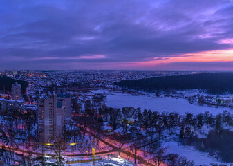 Sunset over the outskirts of the city of Kyiv and snow-covered forest in winter. Kyiv, Ukraine