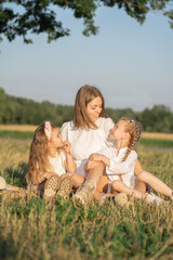 Mother and daughters relax in nature. Vertical photo of a mother with children. Family photo shoot in the village in the field. Psychology of the relationship between mother and child