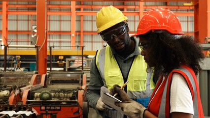 Two engineer worker together, Woman talking and pointing with Man. Two people wear safety uniform...