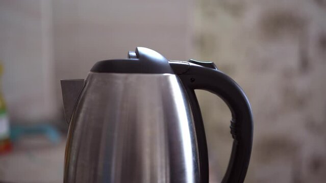 Button for turning on the electric kettle for boiling water. An electric kettle boils water. Person turns on the electric kettle.
