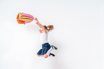 happy schoolgirl in uniform with a backpack jumps on a white background in the studio. the little...