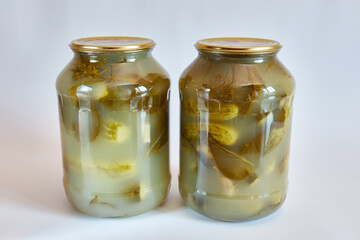 Glass jars with canned cucumbers on a white background.