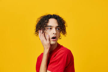 Fototapeta na wymiar Shocked confused funny Caucasian young man in red t-shirt touches cheeks posing isolated on over yellow studio background. The best offer with free place for advertising. Emotions for everyday concept