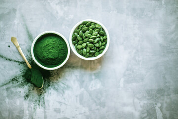 spirulina powder and tablets in white plates on concrete background