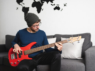 Man concentrated on playing bass while sitting on the sofa of his living room