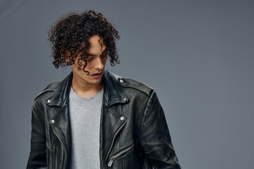 Obraz premium Serious adorable stylish tanned curly man leather jacket looks aside posing isolated on over gray studio background. Cool fashion offer. Huge Seasonal Sale New Collection concept. Copy space for ad