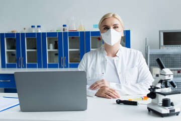 Fototapeta na wymiar Scientist in protective mask looking at camera near microscope and laptop in lab.