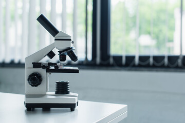 Microscope on white table in blurred laboratory.
