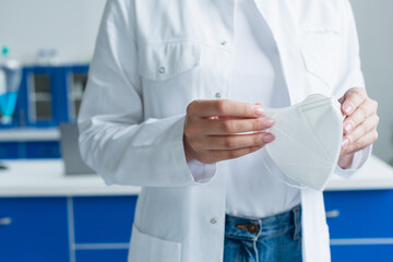Cropped view of scientist holding medical mask in lab.