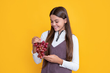 happy child hold fresh grapes bunch on yellow background