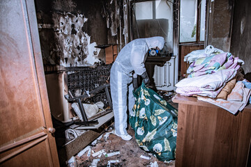 a specialist in a protective suit from a cleaning company cleans a destroyed housing after a fire