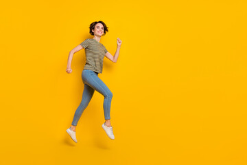 Fototapeta na wymiar Full length photo of excited pretty girl dressed green t-shirt jumping high running empty space isolated yellow color background