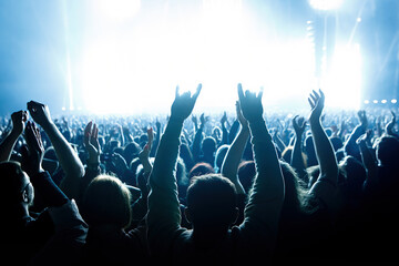 Performance of a popular group. The crowd with raised hands against the stage light.