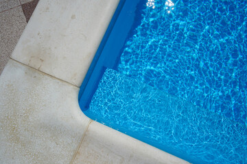 Swimming pool with blue water outdoors with stone gray edge, closeup. Top view.