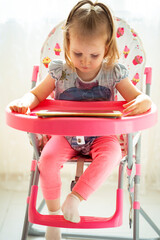 Cute little girl using digital tablet while sitting in baby feeder 