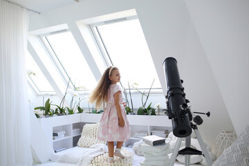 Happy Caucasian girl playing in the room on the attic floor where there is a telescope for the stars. Scandinavian style in the interior. Hobby. Equipment and technologies. Modern concept interior.
