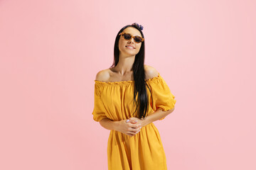 Portrait of young beautiful girl, student in summer yellow dress isolated on pink background. Concept of beauty, art, fashion, human emotions