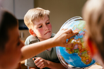 Cute pupil boy with blush on cheeks enthusiastically examines the globe together with other...