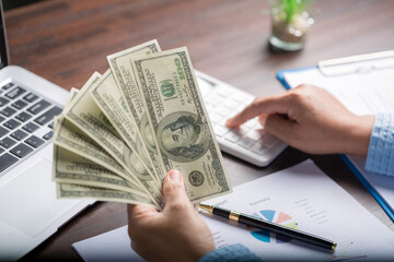 Close up young business woman using counting cash money one hundred dollar bills, checking financial documents