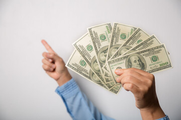 Close up woman holding dollars happy pointing with hand and finger to the side successful, showing money and boasting lottery winning, big profit. indoor studio shot isolated on gray background