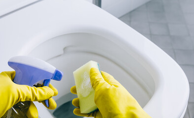 Hands in yellow rubber gloves cleaning toilet