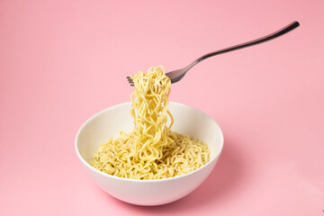 Boiled instant noodles on a pink background. Fork with noodles in the air. Fast food. Modern food.