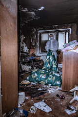 a specialist in a protective suit from a cleaning company cleans a destroyed housing after a fire