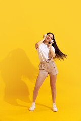 Studio shot of young charming girl with long dark hair in shorts and t-shirt isolated on bright yellow background. Concept of beauty, art, fashion