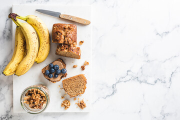 Banana bread with walnuts cut into slices on a marble background. Table top view, copy space for design or text elements