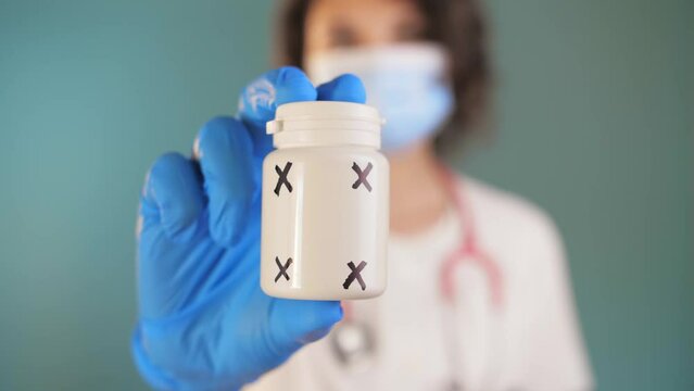 Woman doctor in a medical mask stands against a blue background and holds out a jar of medicine to the camera.Female holding a medicine jar.Slow Motion