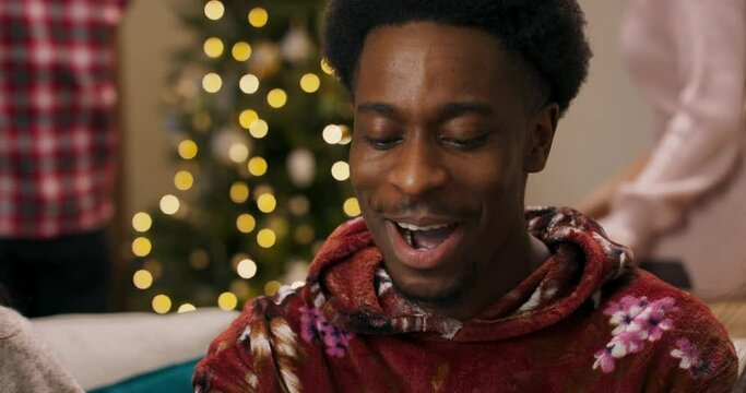 The magic of Christmas Eve. A young man of African appearance received gift and opened it. The guy is pleasantly surprised to receive the long-awaited gift. Friends rejoice for friend.
