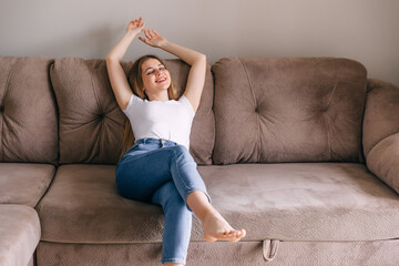 Relaxed young woman leaned on sofa with closed eyes, putting her hands behind her head