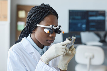 Portrait of young African American woman wearing magnifying visor and inspecting hardware part in engineering laboratory © Seventyfour